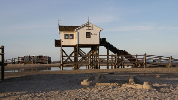 A wooden pier with a small white building on stilts, a wooden walkway, and a sandy beach. - Reihenhaus, St. Peter - Ording (St. Peter-Ording)