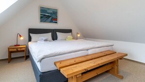 A bedroom with a bed, a bench, a nightstand, and a painting on the wall.