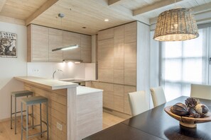 Een moderne keuken met houten kastjes, een centraal eiland, barkrukken en een eettafel voor vier personen.