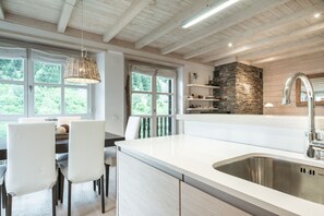 Een moderne keuken met een groot eiland, witte kastjes en een wand met steen decoratie.