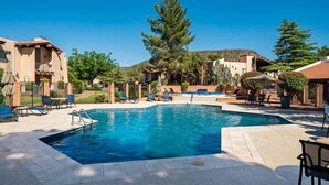 Una piscina con sillones de descanso, rodeada de edificios de estilo arquitectónico mediterráneo.