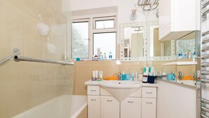 A bathroom with a bathtub, a vanity with a mirror, and toiletries on the counter.