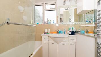 A bathroom with a bathtub, a vanity with a mirror, and toiletries on the counter.