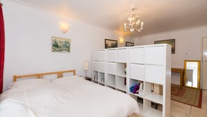 A bedroom with a bed, white wardrobe, wall-mounted light, chandelier, and a painting.