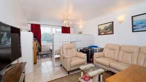 A living room with a television, beige sofas, a glass coffee table, and luggage.