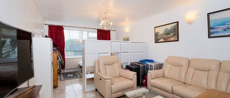 A living room with a television, beige sofas, a glass coffee table, and luggage.