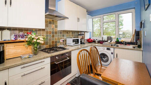 A modern kitchen with white cabinets, a microwave, a stove, and a sink. There is a window providing natural light and a view of the outdoors.