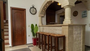 A bar area with a stone counter and wooden stools, a wooden door, and a potted plant. - Modern holiday home in Stalos with balcony (Stalos)