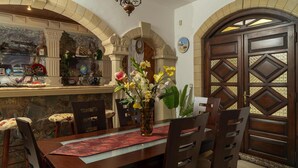 A dining area with a stone wall, a wooden table, chairs, and a decorative vase with flowers. - Modern holiday home in Stalos with balcony (Stalos)
