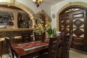 A dining area with a stone wall, a wooden table, chairs, and a decorative vase with flowers. - Modern holiday home in Stalos with balcony (Stalos)