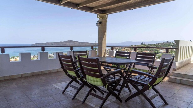 A covered outdoor patio with a round table and chairs, overlooking a coastal view. - Modern holiday home in Stalos with balcony (Stalos)