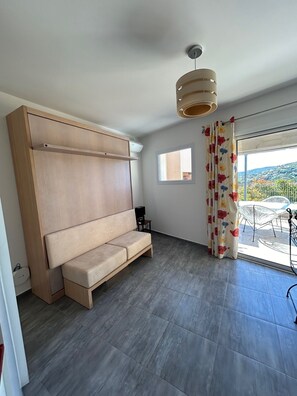 Een moderne kamer met een ingebouwde bank, een tafeltje met een speaker, een raam met uitzicht op de omgeving, en een plafondlamp.