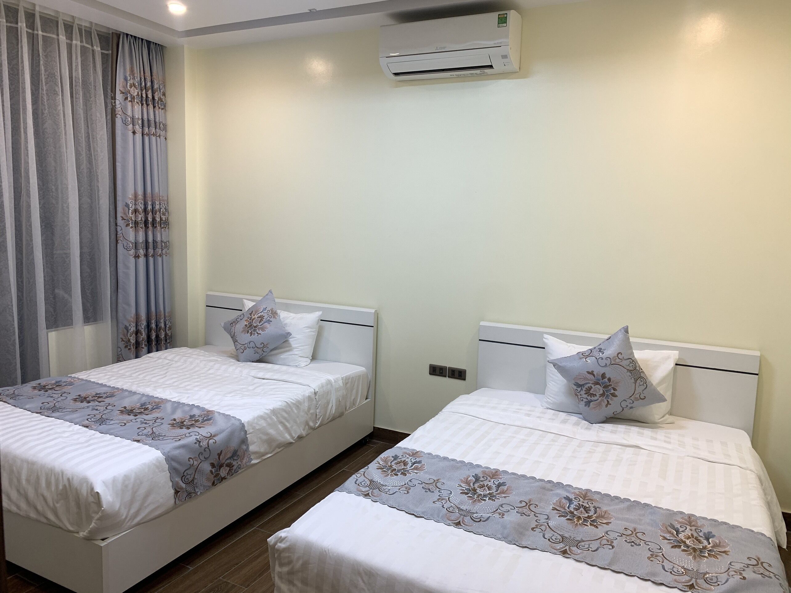 A hotel room with two beds, each with a floral-patterned bedspread and matching pillows. An air conditioning unit is mounted on the wall above the beds.