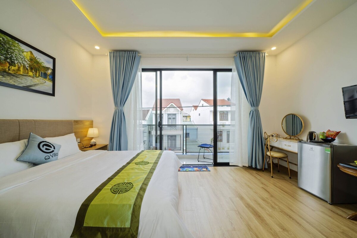 A hotel room with a bed, a desk, a chair, a small fridge, and a view of the outside.