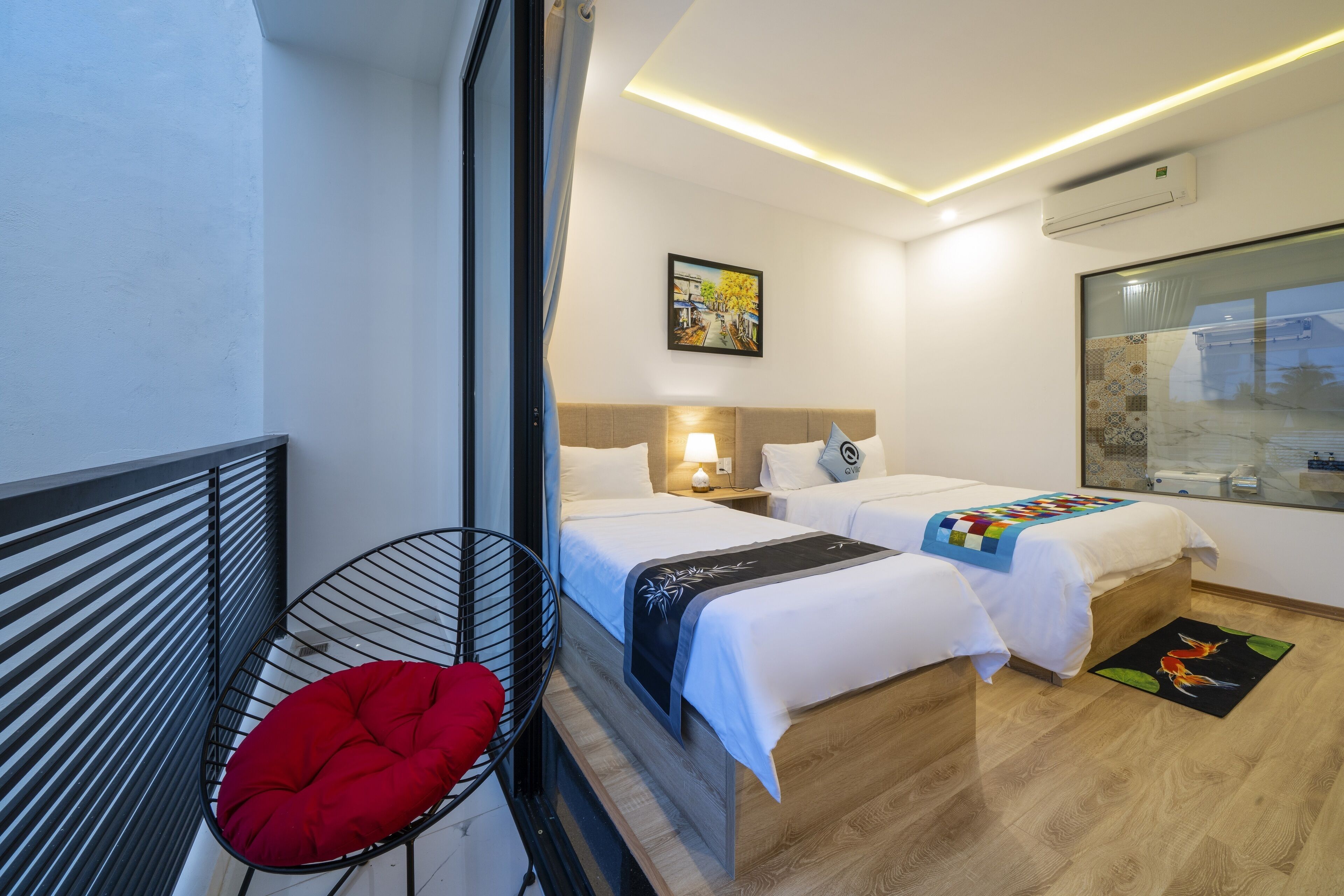 A hotel room with two beds, a red chair, a painting on the wall, and a window with a view.