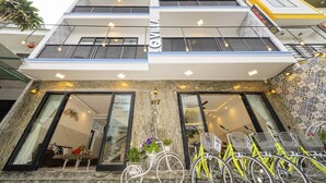 A multi-story building with a modern design, featuring balconies, large windows, and a ground-level entrance with a bicycle rental station. - Q Villa Hoi An (Da Nang)