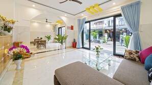 A modern hotel lobby with a reception desk, seating area, and large windows offering a view of the street. - Q Villa Hoi An (Da Nang)