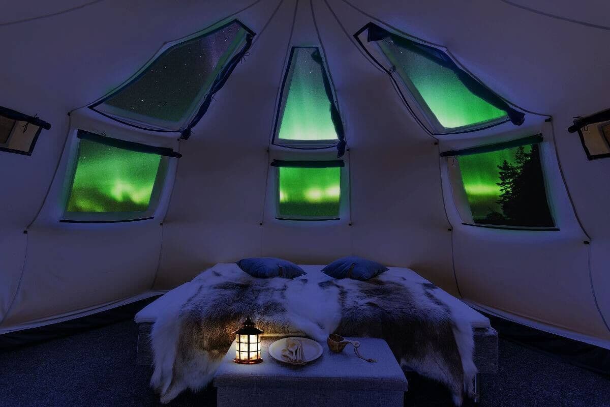 Ein gemütliches Zimmer mit einem Bett, einer Laterne und Blick auf das Polarlicht durch Dachfenster.