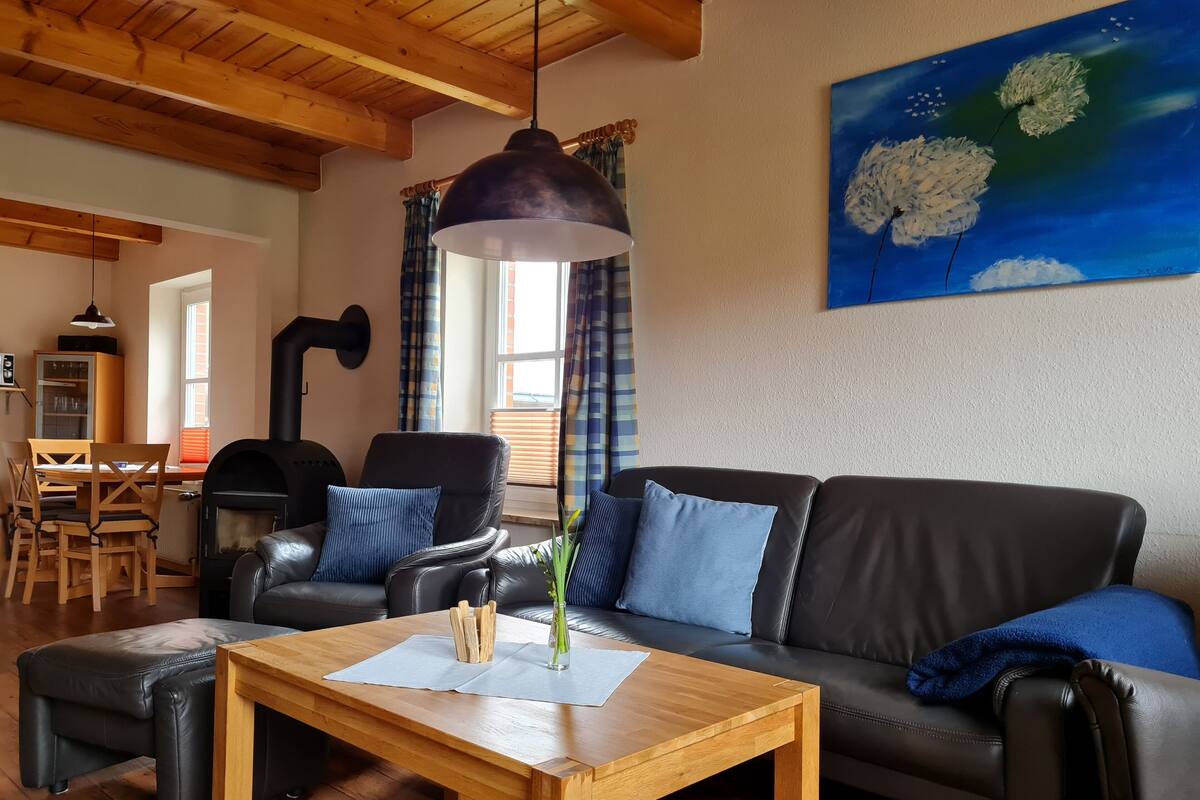 Ein gemütliches Wohnzimmer mit Holztisch, Ledersofa und einem Blumenbild.