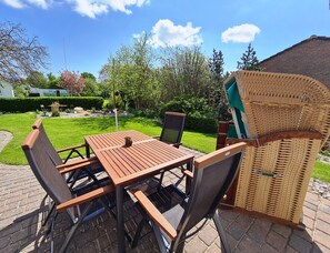 A patio with a wooden table and chairs, a wicker chair, and a small table with a speaker.