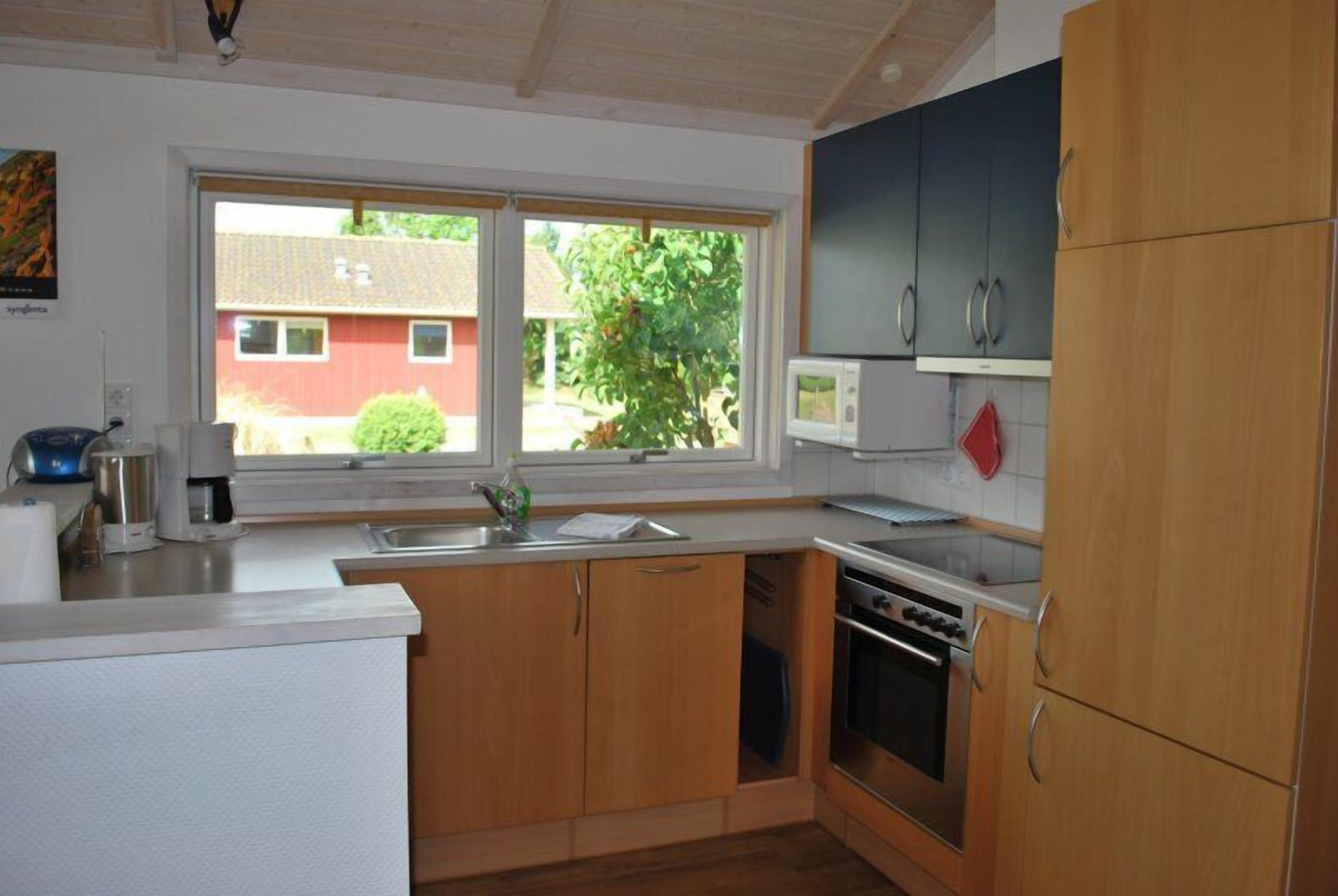 A kitchen with wooden cabinets, a microwave, a stove, and a window with a view of a house and greenery.