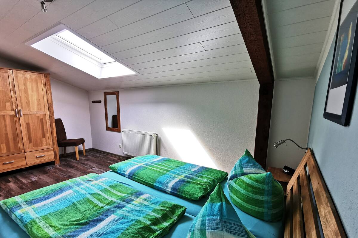 Ein Schlafzimmer mit zwei Einzelbetten, einem Holzschrank, einem Stuhl, einem Heizkörper und einem Oberlicht.