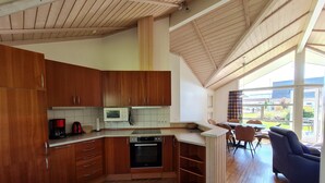 Une cuisine moderne dotée de meubles en bois, d’un four à micro-ondes, d’une machine à café et d’un four traditionnel. On y trouve également un coin repas avec une table et des chaises, ainsi que de grandes fenêtres offrant une vue sur l’extérieur.