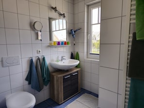A bathroom with a white toilet, a sink with a wooden cabinet, a mirror, and a window.