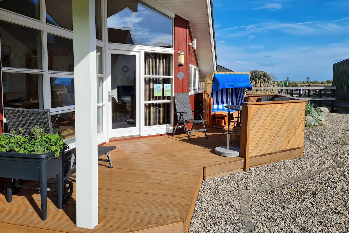 Eine Holzterrasse mit Gartenmöbeln, einem überdachten Sitzbereich und Blick auf die umliegende Landschaft.