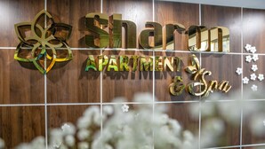 «Sharm Apartment & Spa» -kyltti, jossa on kukka-aiheinen kuvio ja kultakirjaimet, on kiinnitetty puiseen seinään.