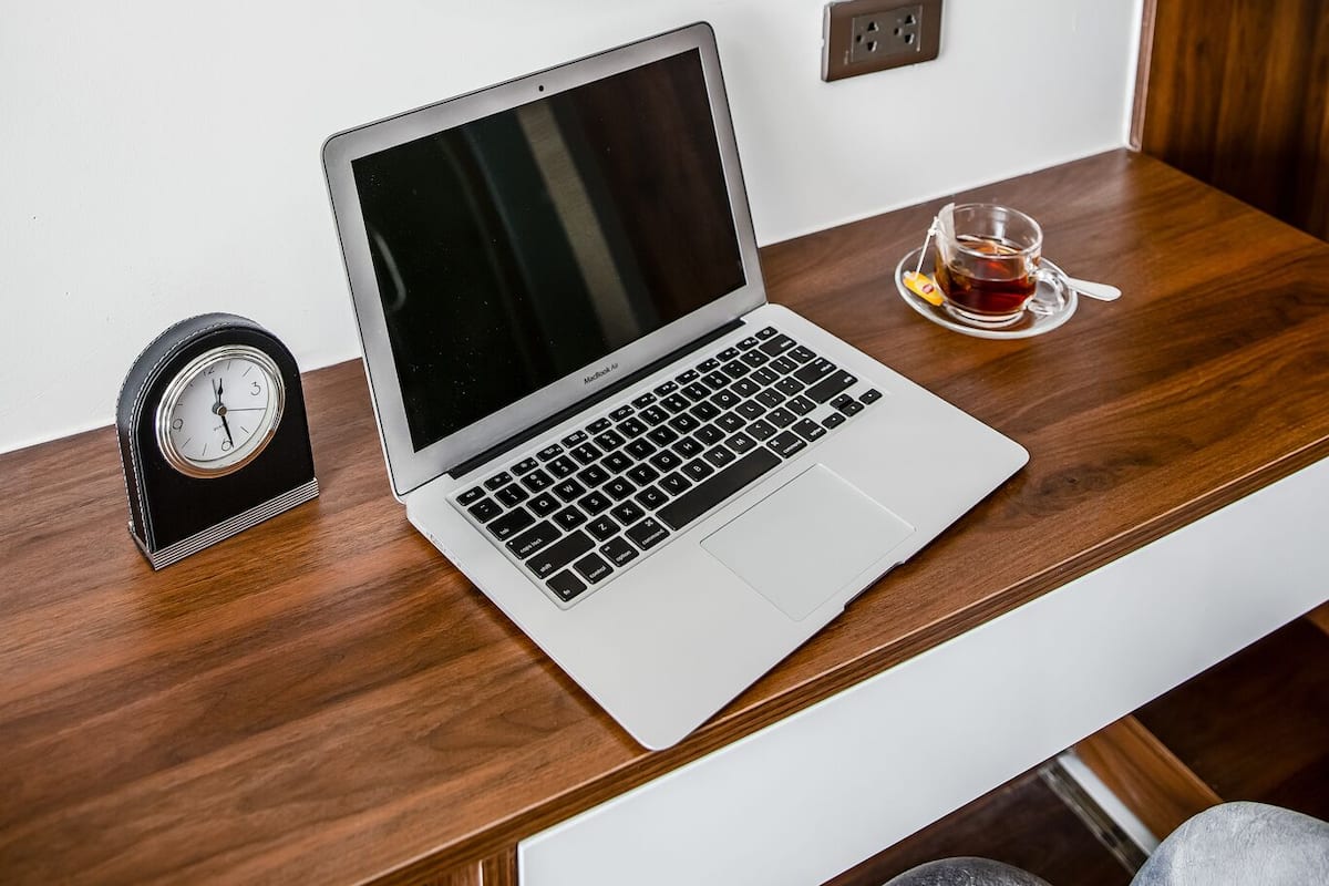A laptop on a wooden desk with a round mirror above it, reflecting a kitchen area.