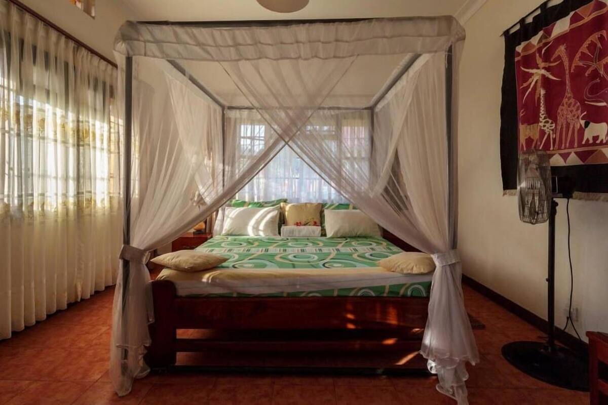 A room with a bed under a canopy, a window with curtains, and a wall with a tapestry.