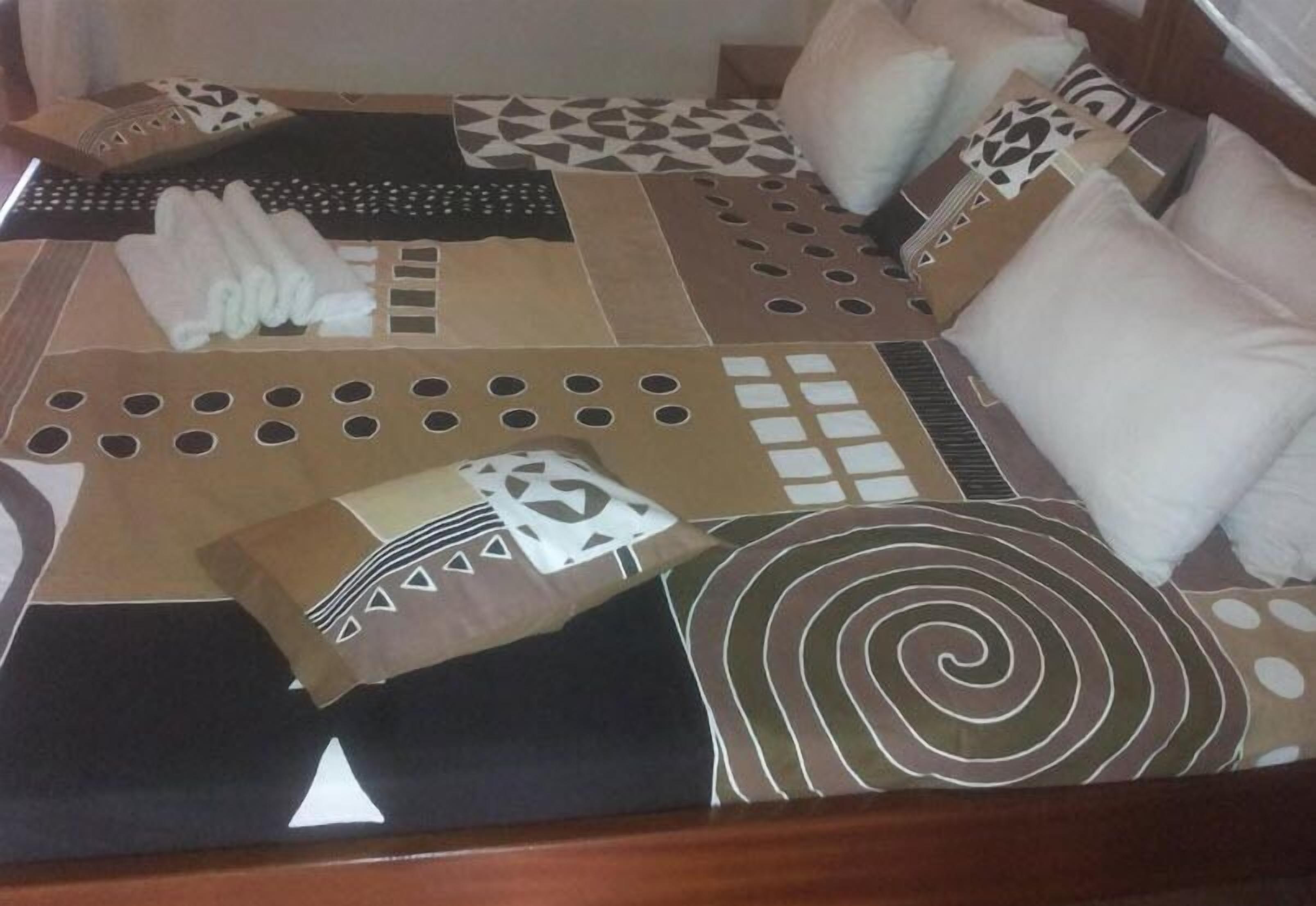 Una cama con una colcha estampada, varios almohadones y una toalla doblada.