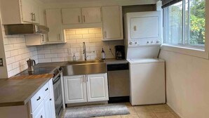 A compact kitchen with white cabinets, a stainless steel sink, a dishwasher, and a window with a view of greenery.