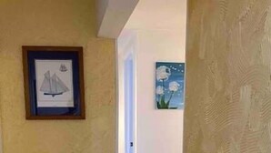 A hallway with tiled flooring, a framed picture of a sailboat on the left, and a textured wall on the right.