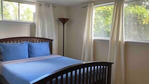 A bedroom with a bed, curtains, a floor lamp, and a window with a view of trees.