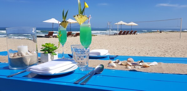 A beach table with drinks, a glass pitcher, and a plate with utensils.