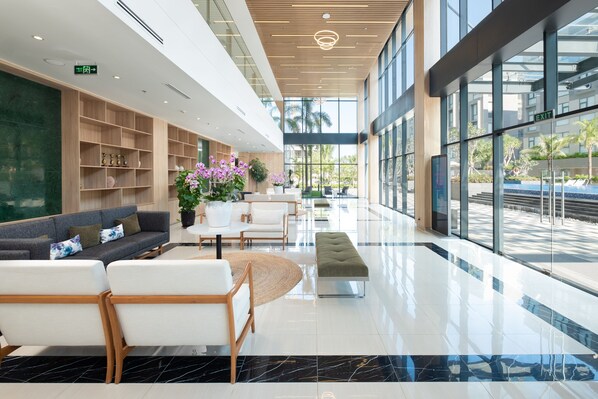A spacious lobby with a modern design, featuring a reception area with a sofa and chairs, a coffee table, and a potted plant.