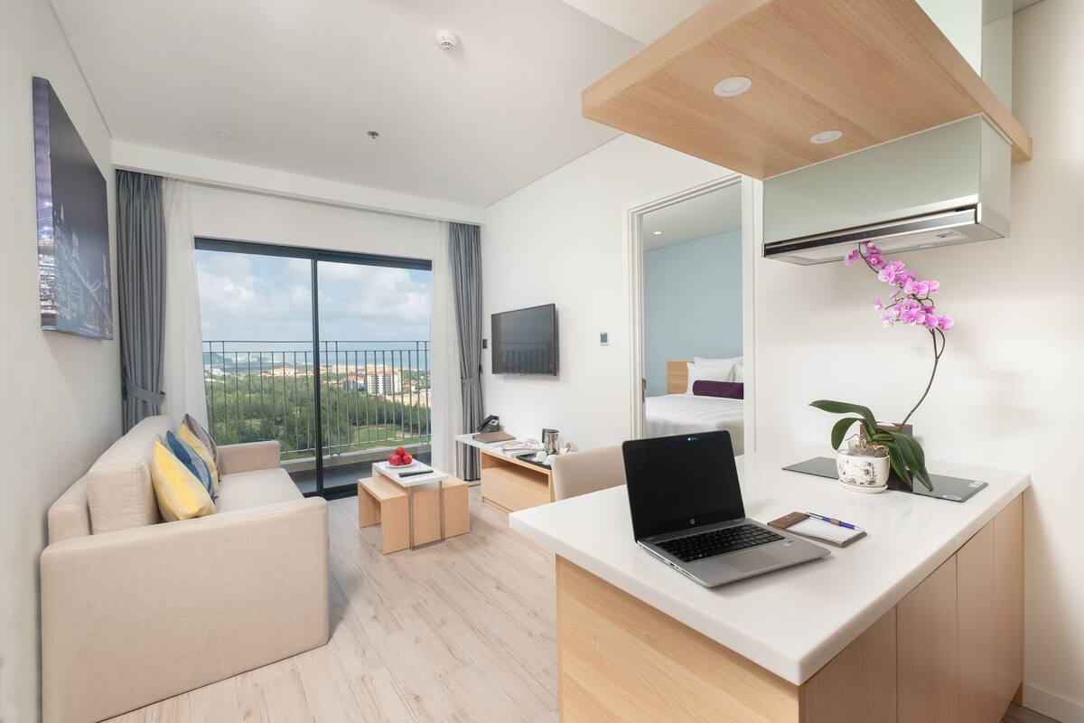 Une chambre d’hôtel moderne dotée d’un balcon, d’un bureau avec un ordinateur portable, d’un lit et d’un grand miroir.