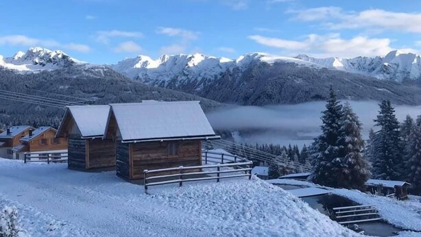 A snow-covered mountain lodge with wooden cabins, a wooden fence, and a view of snow-capped peaks in the background. - Ferienhaus Fanningberg (Weisspriach)