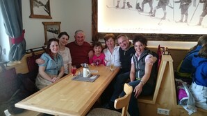 A family seated at a wooden table with drinks, in a room with a wooden bench and a framed picture on the wall. - Ferienhaus Fanningberg (Weisspriach)