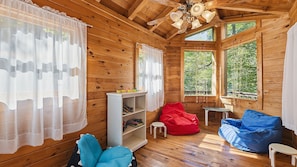 A wooden cabin interior with a wooden floor, a bookshelf, a red bean bag, a blue bean bag, and a small table. - Views, privacy, Kids Playhouse, Easy Access, Fast WiFi! Gated community (Waynesville)