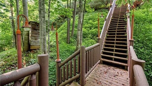 A wooden staircase in a forested area with railings and a wooden structure in the background. - Views, privacy, Kids Playhouse, Easy Access, Fast WiFi! Gated community (Waynesville)