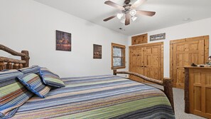 A bedroom with a bed, a ceiling fan, wooden wardrobe, and a window with blinds. - Views, privacy, Kids Playhouse, Easy Access, Fast WiFi! Gated community (Waynesville)