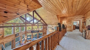Ein Holzhütten-Interieur mit Balkon, großen Fenstern und einer Treppe.