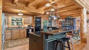A rustic kitchen with wooden cabinets, a central island, and a hanging light fixture. - Views, privacy, Kids Playhouse, Easy Access, Fast WiFi! Gated community (Waynesville)