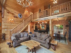 Relax in a cabin-style room with a spacious L-shaped sofa, wooden coffee table, and staircase to an upper level.