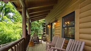 A wooden porch with rocking chairs and a broom, overlooking a forested area. - Views, privacy, Kids Playhouse, Easy Access, Fast WiFi! Gated community (Waynesville)
