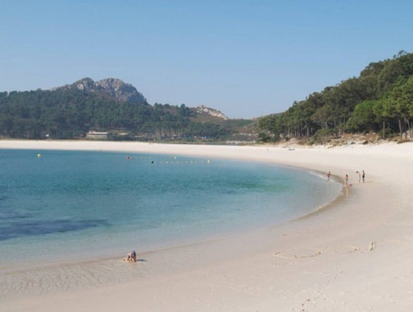 A beach with clear water, a sandy shore, and a forested hill in the background. - Sea view house (Cangas)