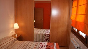 Een slaapkamer met een bed, een nachtkastje, een lamp, een raam met gordijnen en een deur die naar een andere kamer leidt.